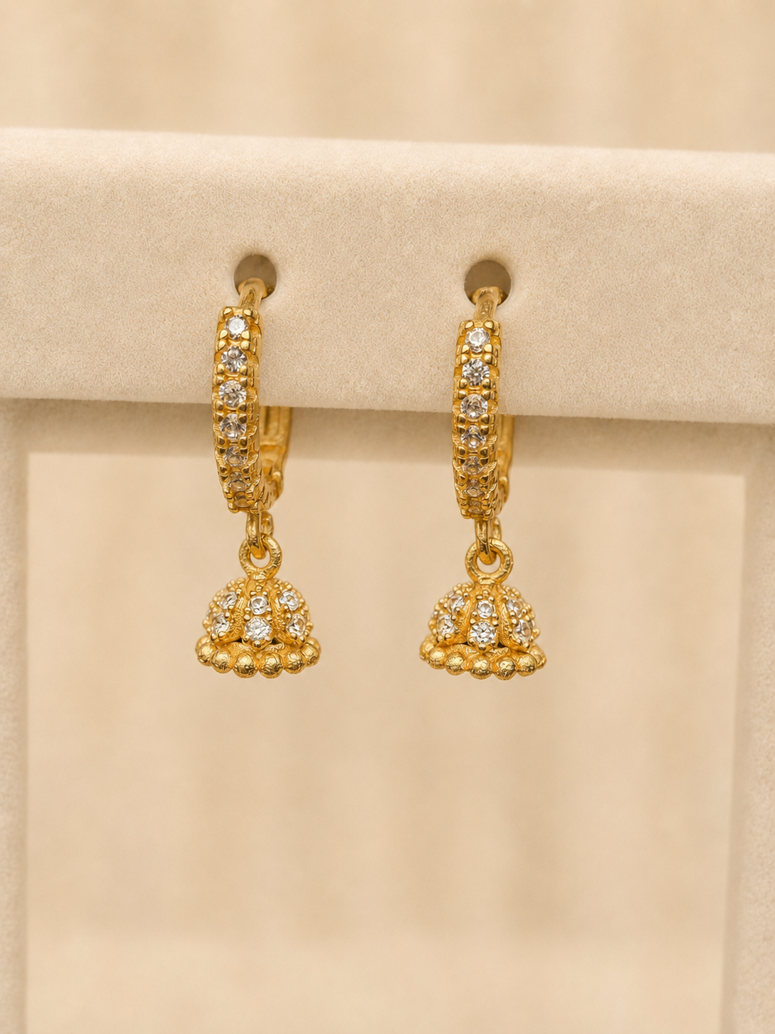 Mishri by Tijori: gold pavé huggie hoops with a small pavé jhumka drop finished with a beaded gold rim, hanging on a cream suede display.